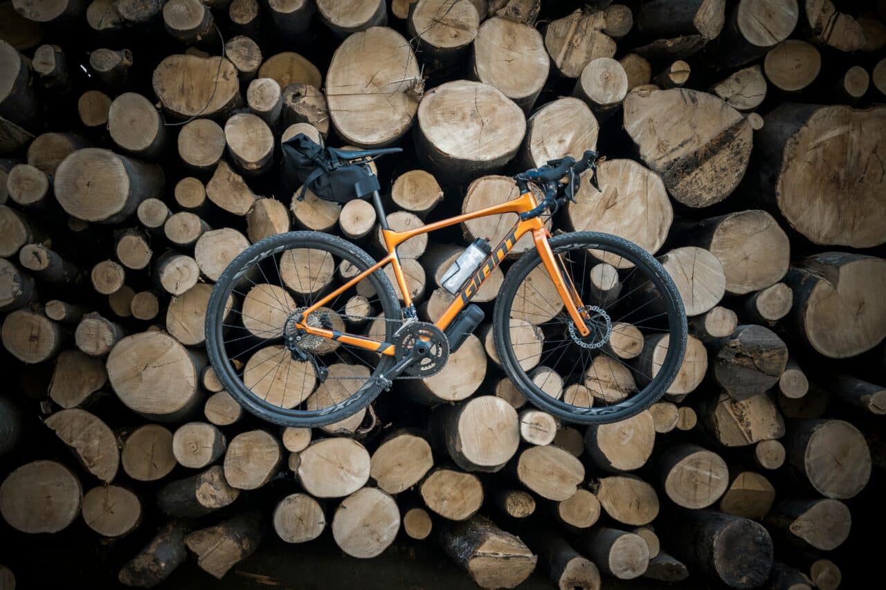 Ein orangenes Gravel Bike auf Baumstämmen platziert.