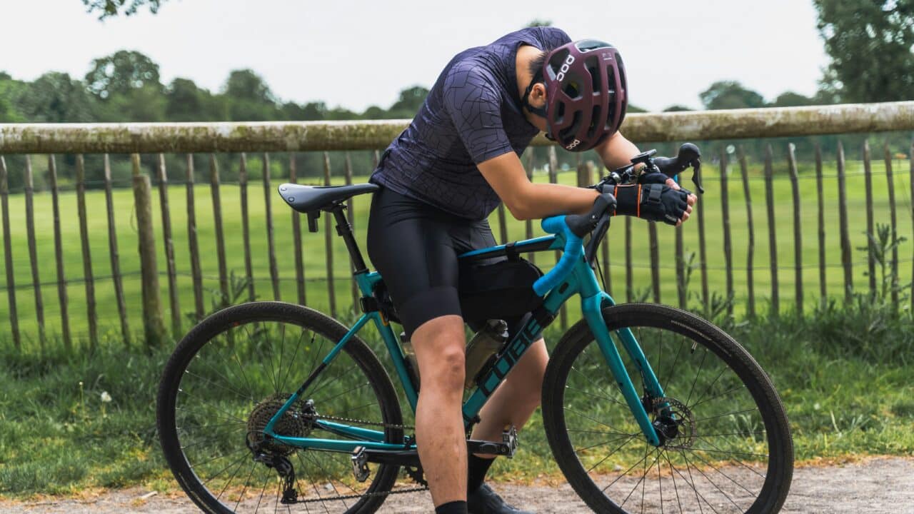 Ein erschöpfter Mann stützt sich auf dem Lenker seines Gravel Bikes ab.